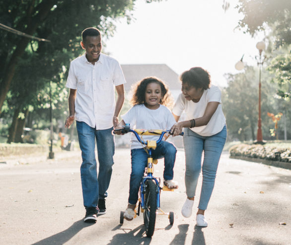 Family teaching child to ride a bike